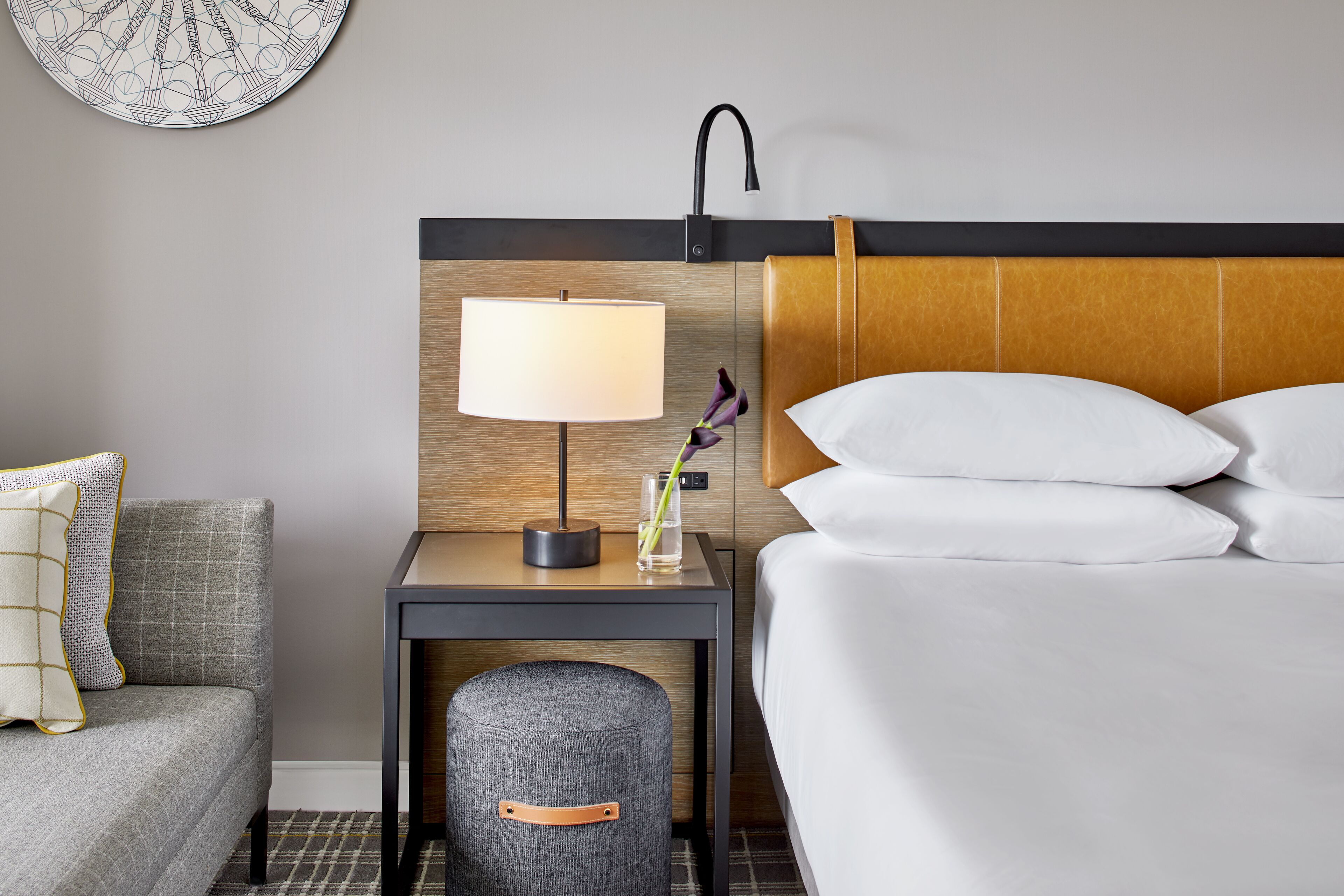 A hotel room with a bed, a nightstand with a lamp, a small table, and a trash bin.