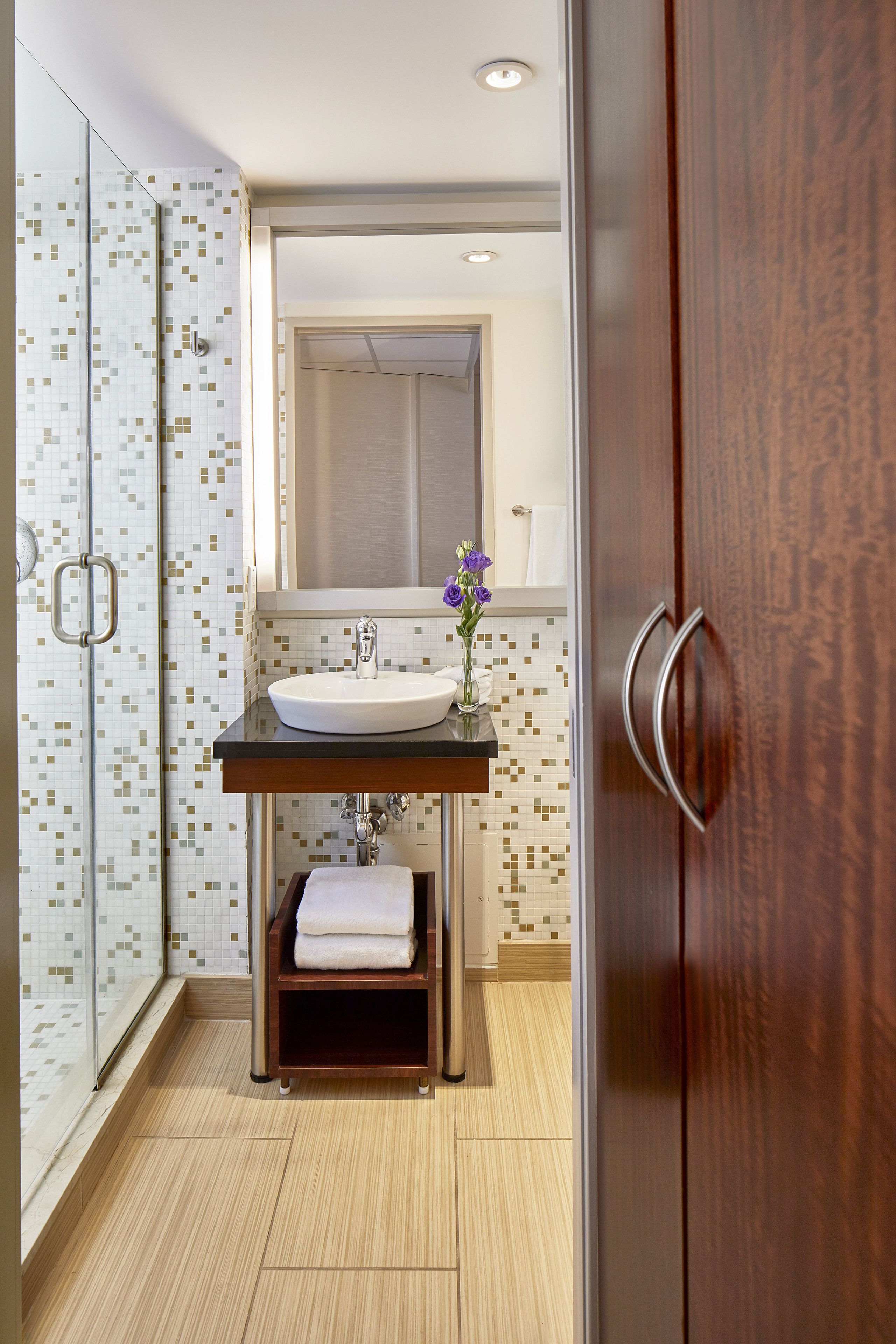 A modern bathroom with a glass shower, a sink with a vase of flowers, and wooden cabinets.