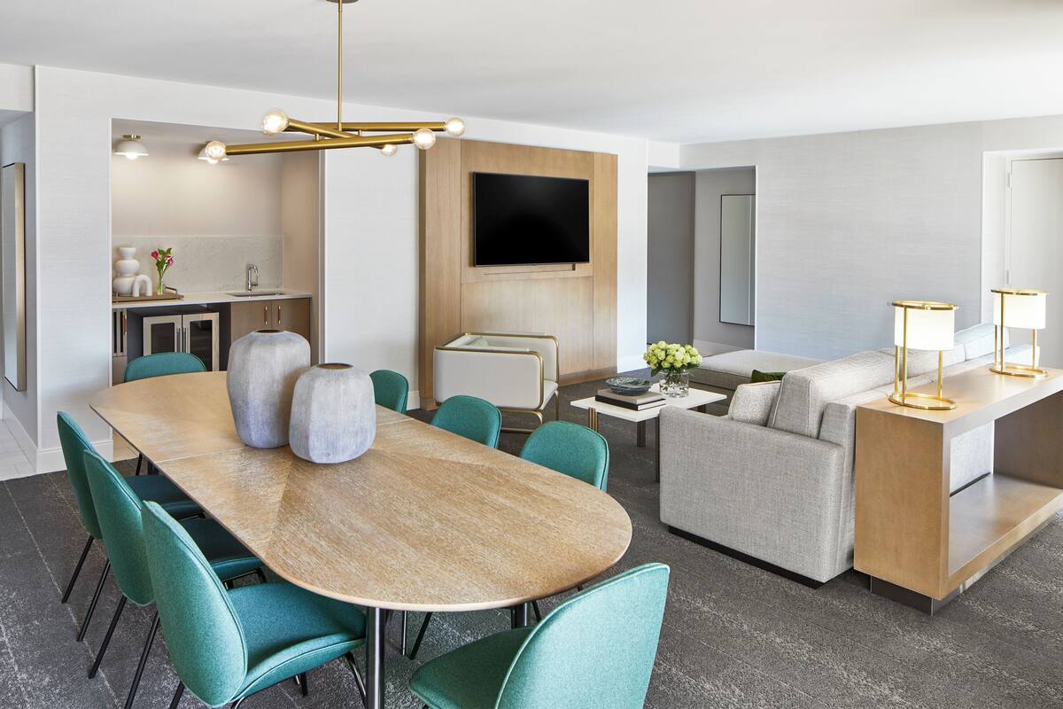 A modern hotel room with a dining area, a sofa, a TV, and a small kitchen.