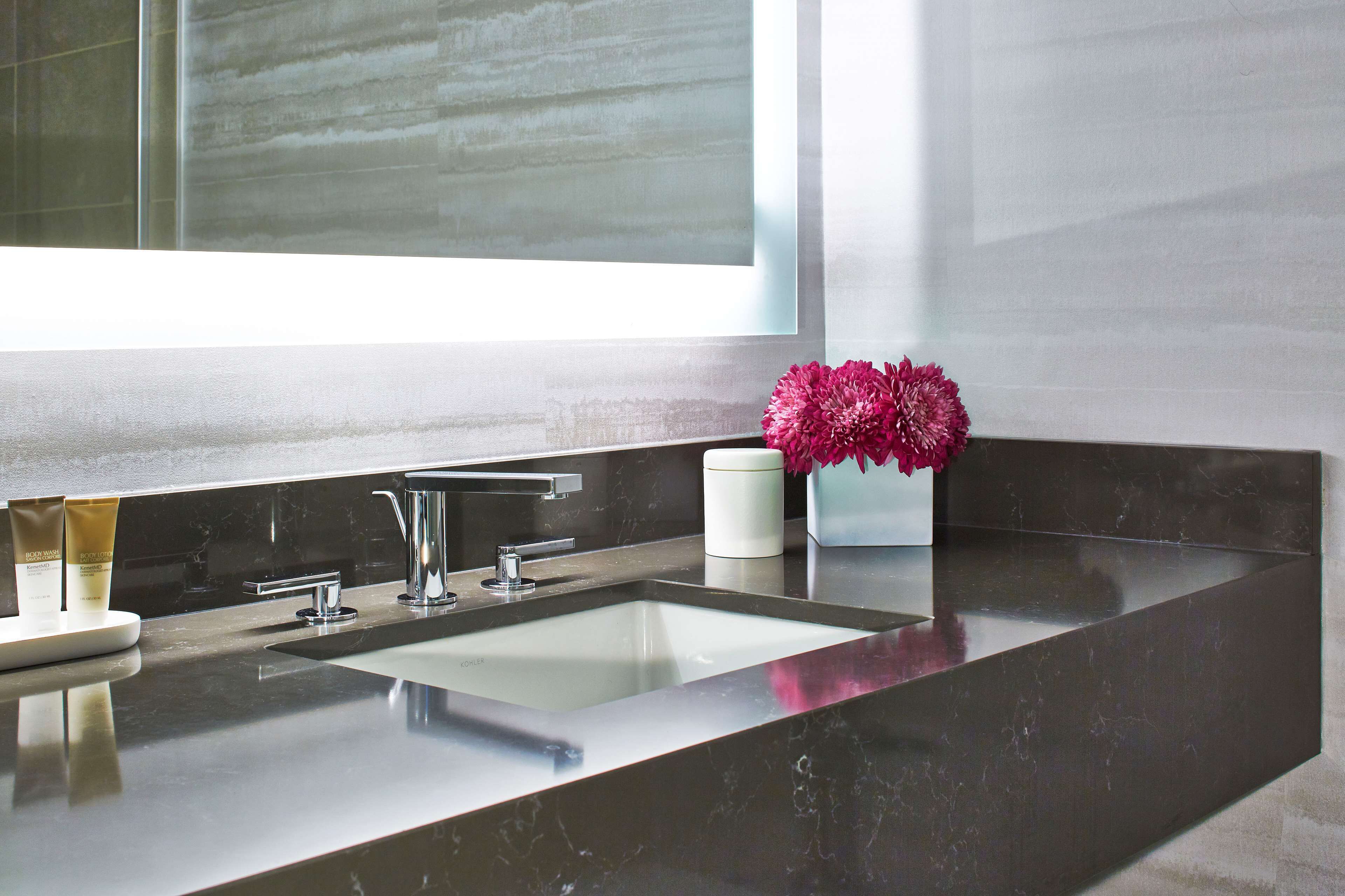 Une salle de bain moderne avec un grand miroir, un lavabo et un vase de fleurs.
