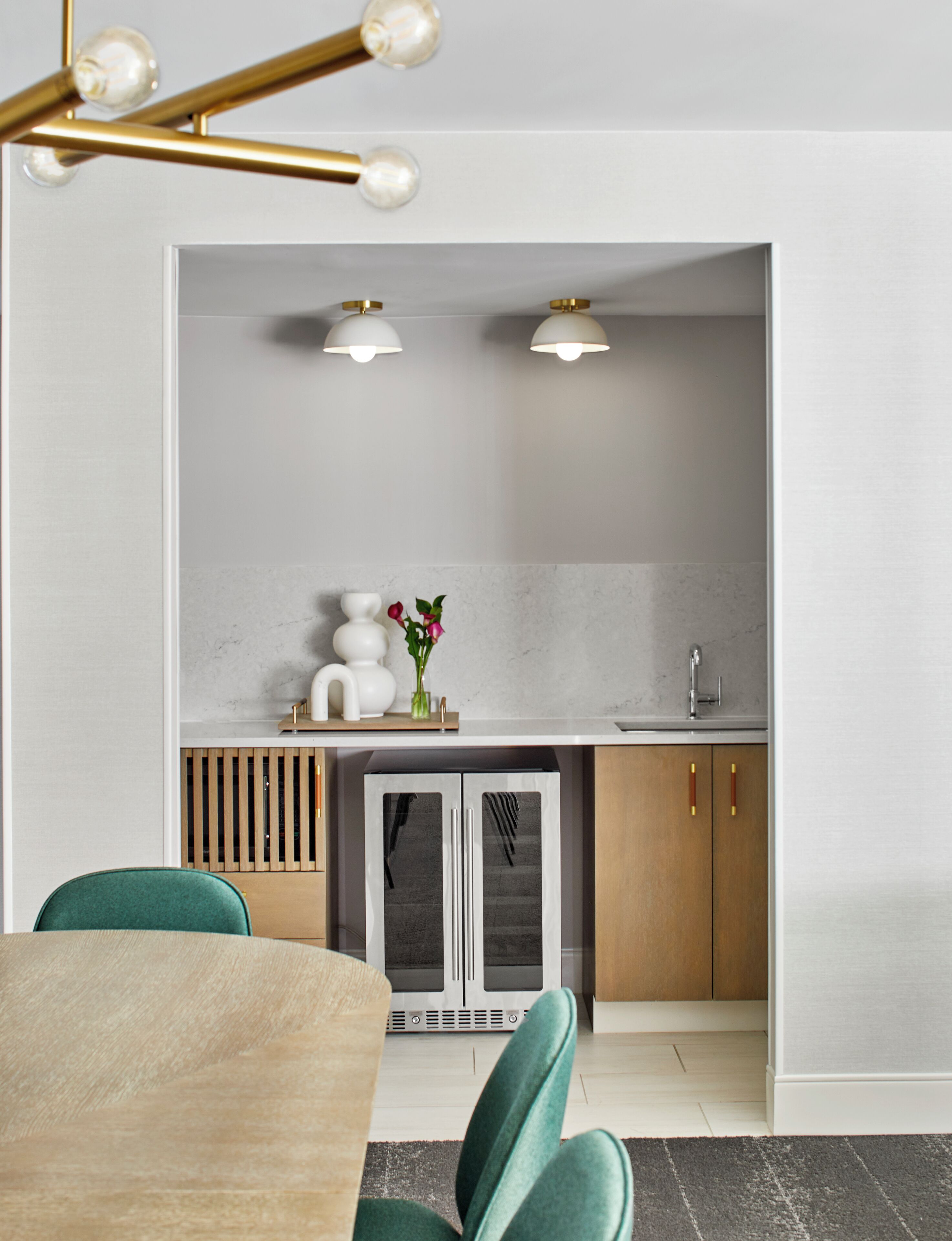 A modern kitchen with a built-in oven, a sink, and a countertop. There is a dining table with chairs and a vase with flowers on the countertop.