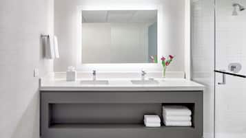 Un baño moderno con un espejo grande, dos lavamanos, una ducha y un estante con toallas.