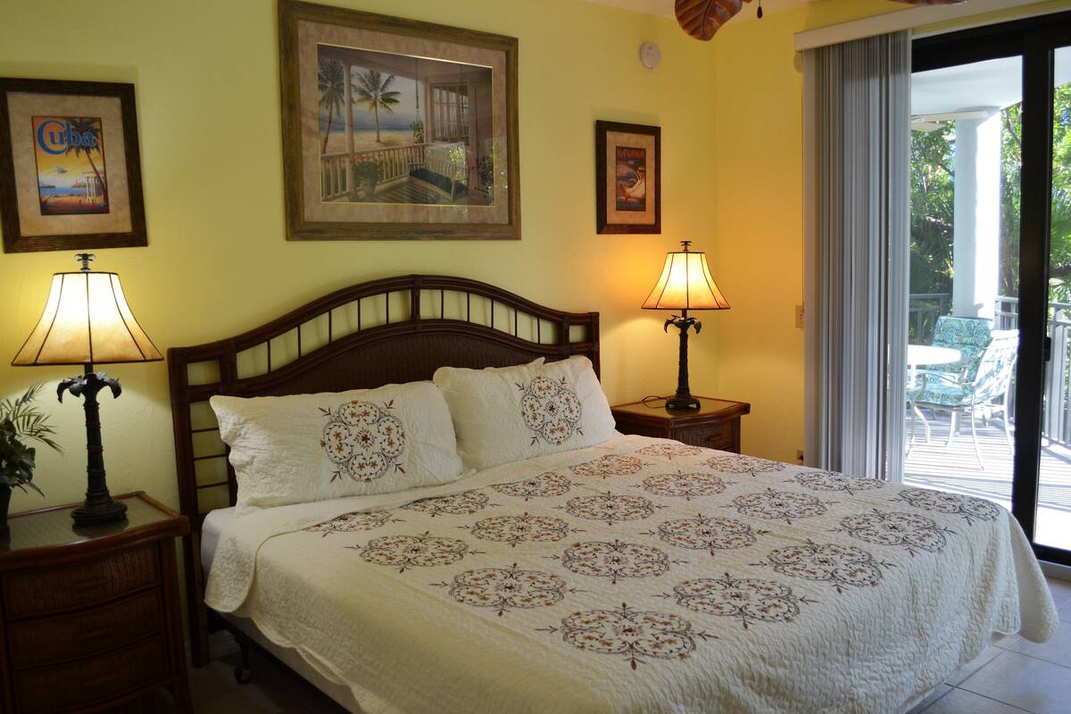 A bedroom with a large bed, two bedside lamps, a wooden headboard, and a balcony with a chair.