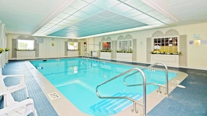 An indoor swimming pool with clear water, a blue tiled floor, and a pool ladder. - Magnuson Grand Pioneer Inn and Suites (Escanaba)