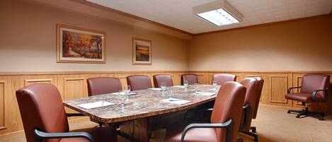 A conference room with a large table, eight leather chairs, and two framed paintings on the walls.