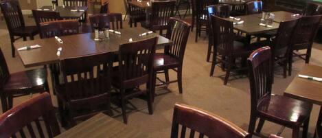 A restaurant with multiple tables and chairs, a television screen, and a clock on the wall.
