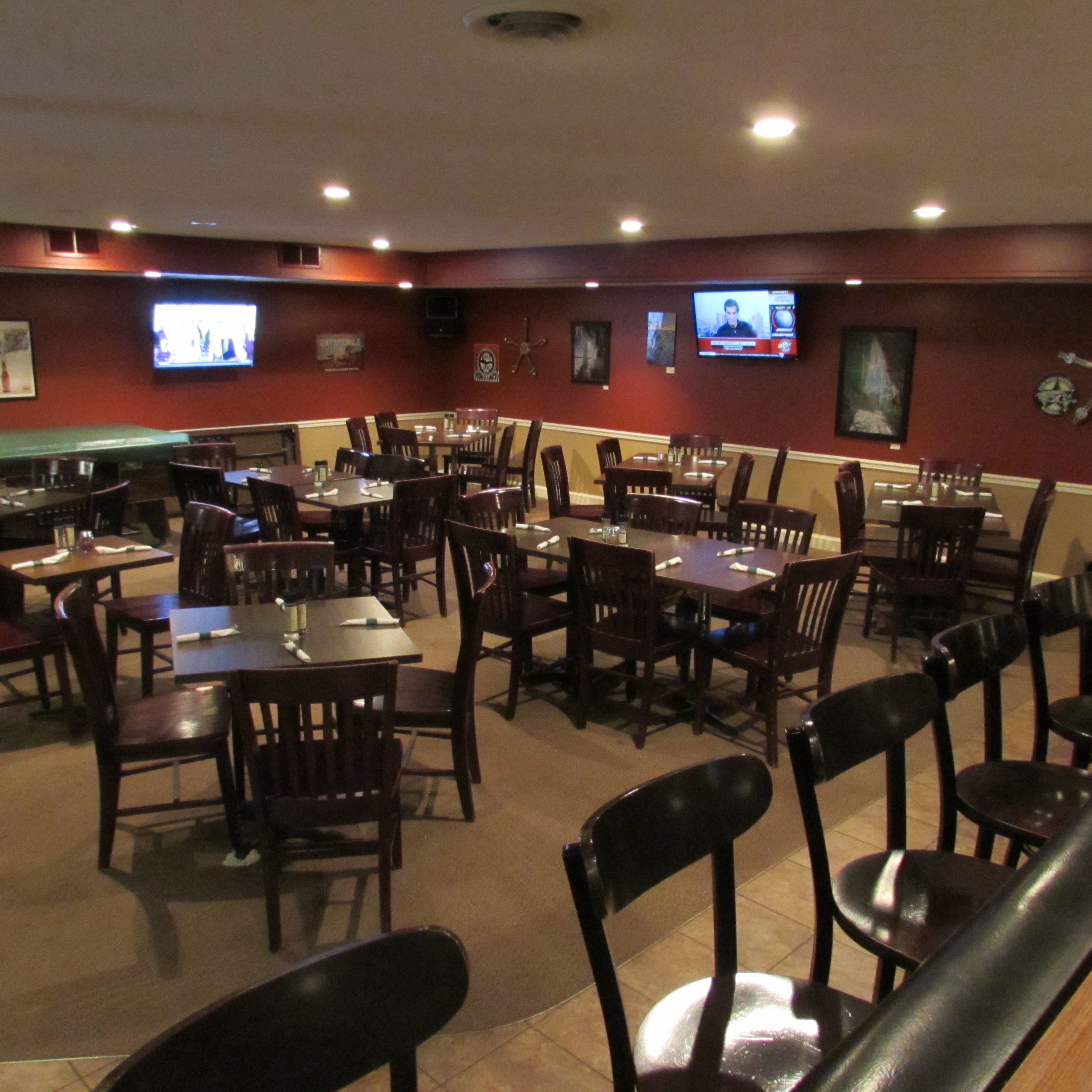 Un restaurante con varias mesas y sillas, una mesa de billar y dos televisores montados en la pared.