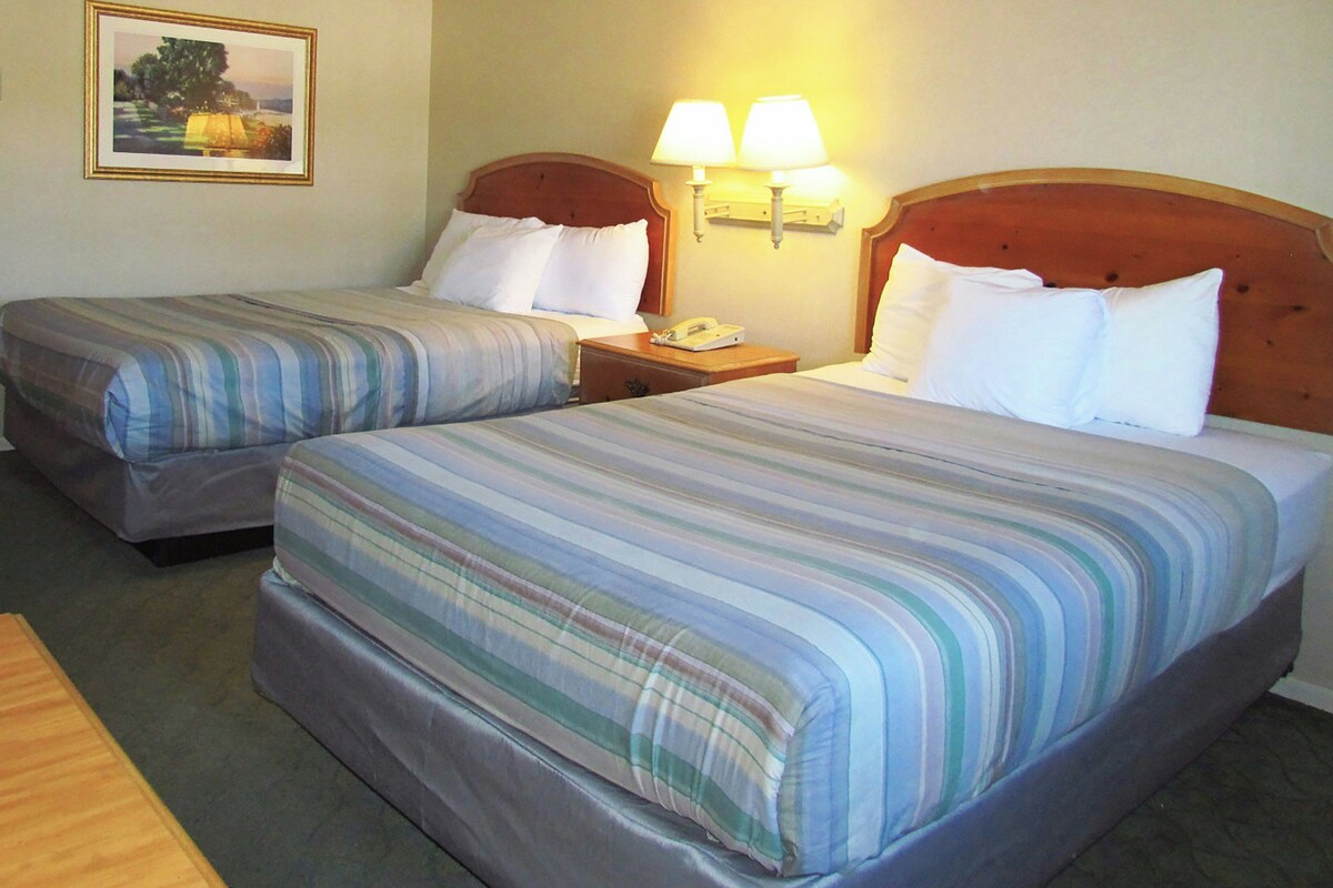 Une chambre d’hôtel avec deux lits, une tête de lit en bois, une table de chevet avec une lampe et un tableau encadré au mur.