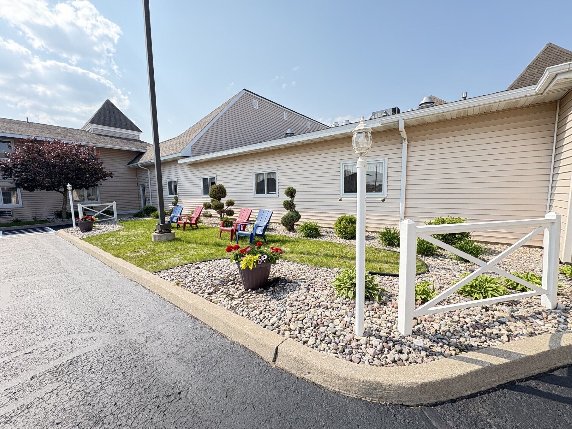 A residential building with a well-maintained lawn, outdoor seating area with chairs, and a small garden with potted plants.