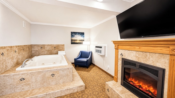 A hotel room with a large bathtub, a fireplace, a flat-screen TV, and a chair. - Magnuson Grand Pioneer Inn and Suites (Escanaba)