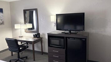 Habitación de hotel con escritorio, silla, televisor, cafetera y microondas.