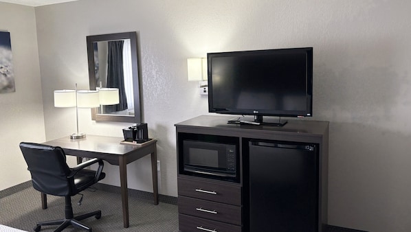 A hotel room with a desk, chair, television, coffee maker, and a microwave.