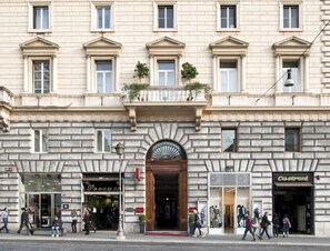 A historic building with a central entrance, multiple windows, and storefronts on the ground floor. - Hotel Giolli Nazionale (Rome)