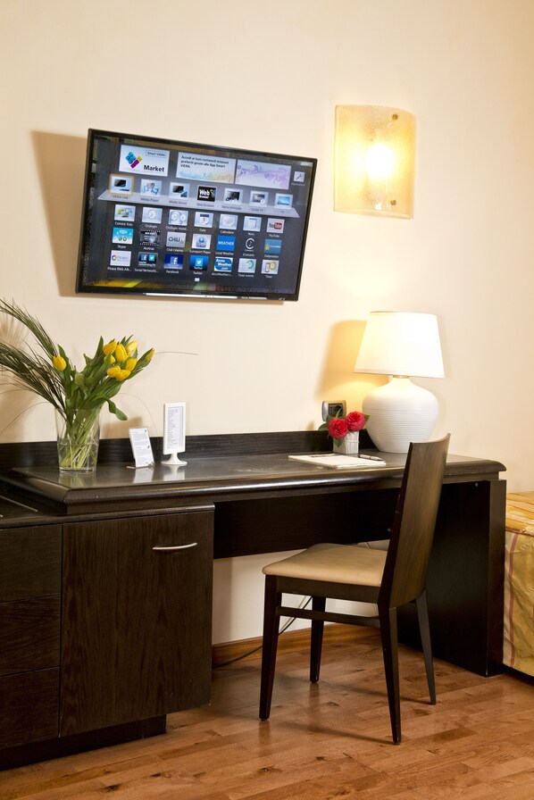 A hotel room with a desk, chair, a flat-screen TV mounted on the wall, a lamp, and a vase with flowers. - Hotel Giolli Nazionale (Rome)