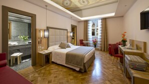 A hotel room with a large bed, a desk with a laptop, a red chair, and a small table. - Hotel Giolli Nazionale (Rome)