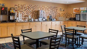 A hotel kitchen with a coffee machine, a waffle maker, and a microwave. There are wooden cabinets and a tiled backsplash. - Baymont by Wyndham Indianapolis East (Indianapolis)