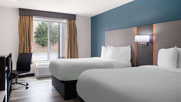 A hotel room with two beds, a desk, a chair, and a large window with curtains. - Baymont by Wyndham Indianapolis East (Indianapolis)