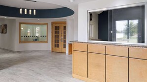 A reception area with a wooden counter, a large window, and a curved ceiling with recessed lighting. - Baymont by Wyndham Indianapolis East (Indianapolis)