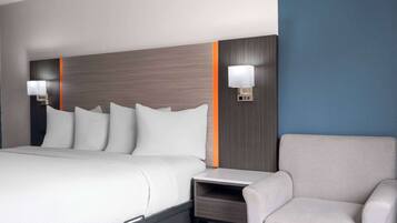Habitación de hotel con una cama grande, dos mesitas de noche con lámparas, una silla y una pequeña mesa.