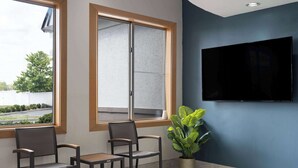 A waiting area with two chairs, a potted plant, and a TV on the wall. - Baymont by Wyndham Indianapolis East (Indianapolis)