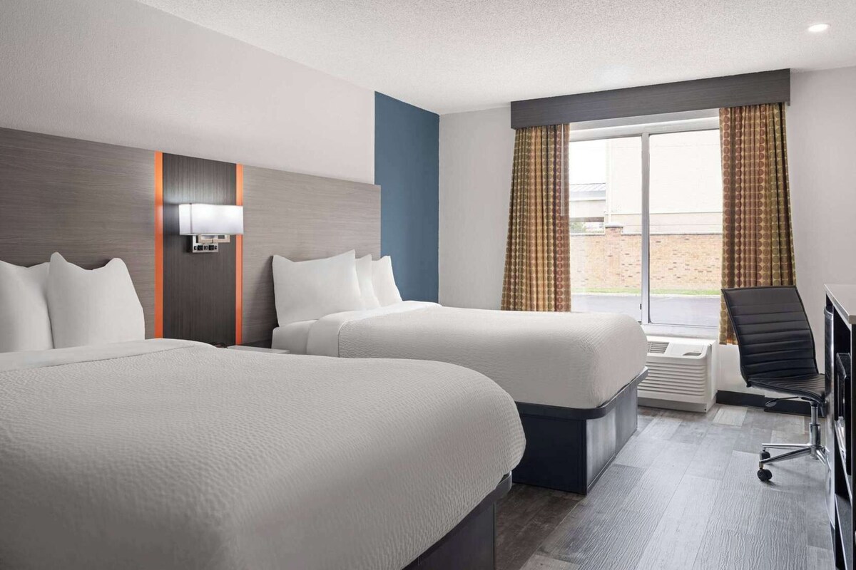 A hotel room with two beds, a desk, a chair, and a window with curtains.