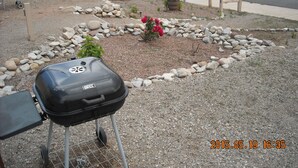 A barbecue grill in a landscaped garden area with a paved road and vehicles in the background.
