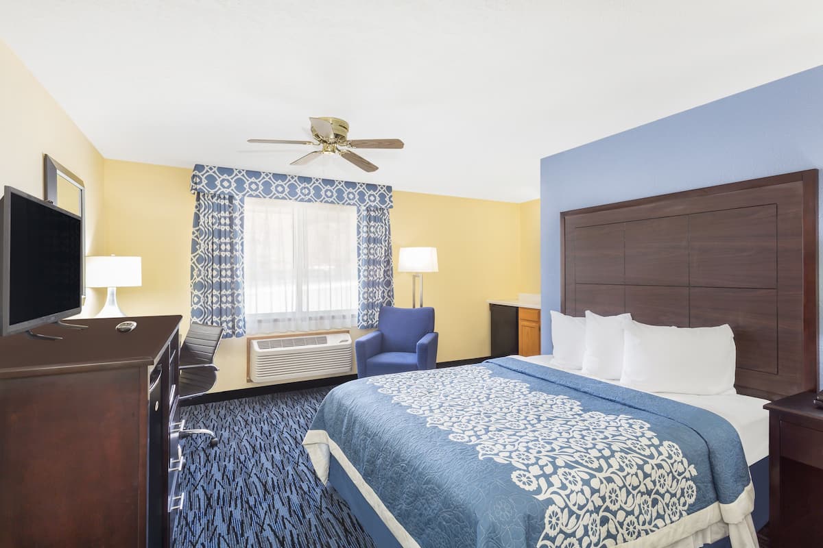 Quarto de hotel com cama, escrivaninha, cadeira, televisão e ventoinha no teto.