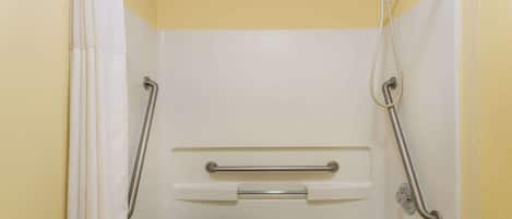 Un baño con ducha, barras de apoyo y un escalón para facilitar el acceso.