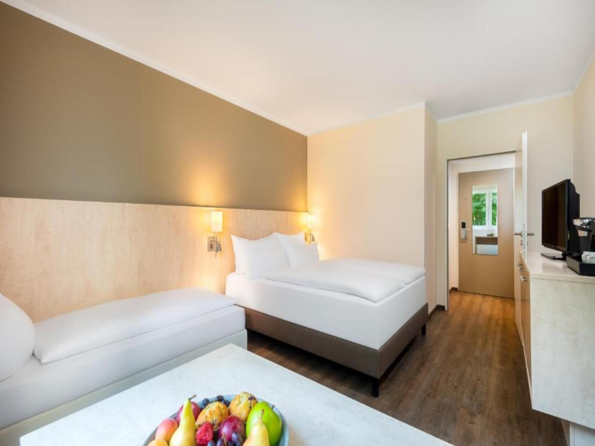 Una habitación de hotel con cama, sofá, una mesita con fruta y televisión.