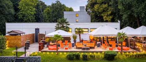 Un área de estar exterior moderna con sombrillas, una escalera que conduce a un edificio y un césped bien cuidado.