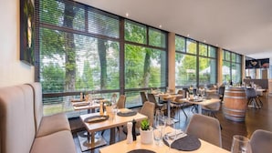 Een restaurant met grote ramen, houten tafels en moderne stoelen.