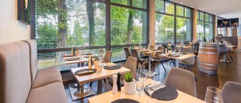 A restaurant with large windows, wooden tables, and modern chairs.