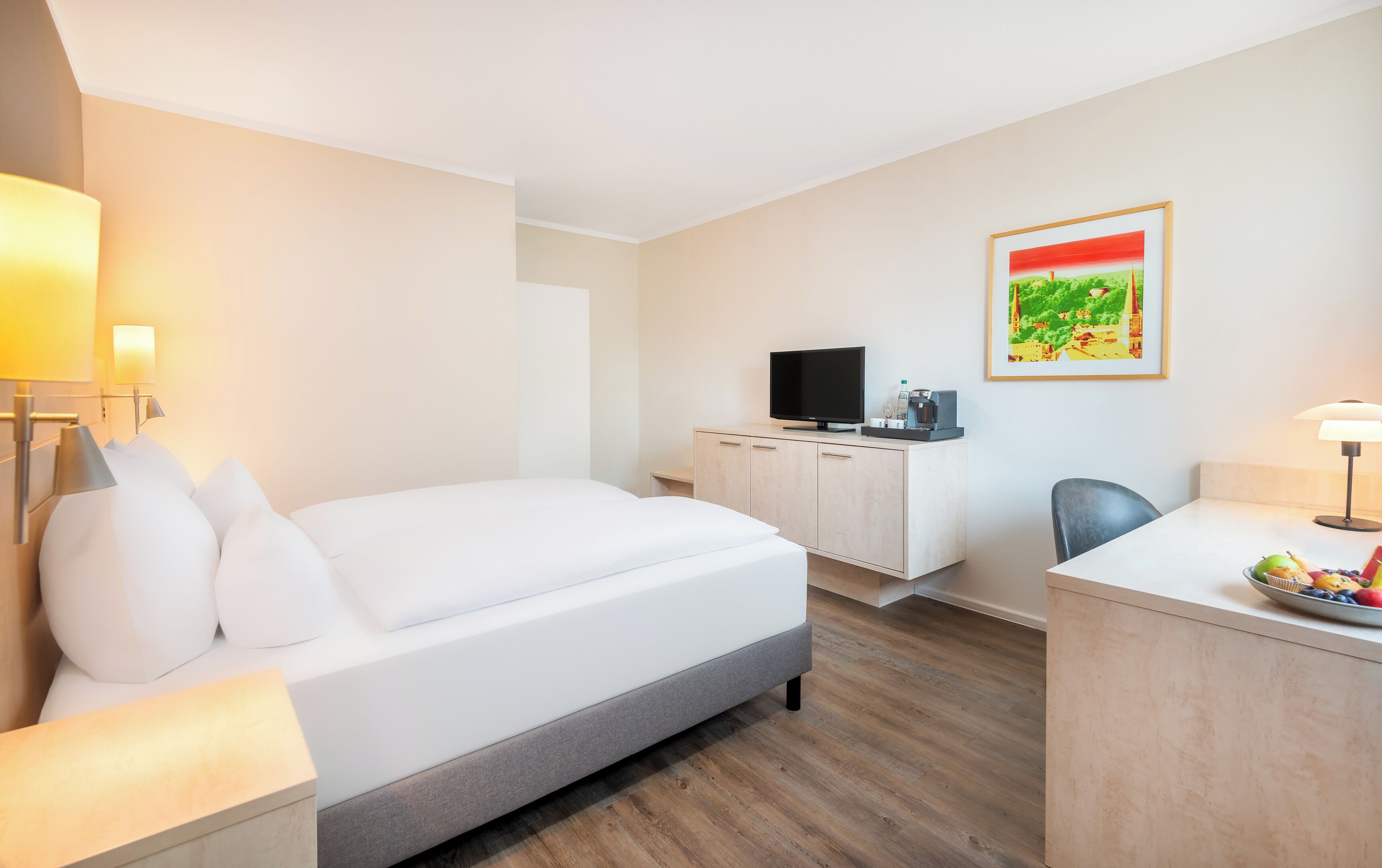 Une chambre d’hôtel avec un lit, un bureau, une télévision et un tableau au mur.