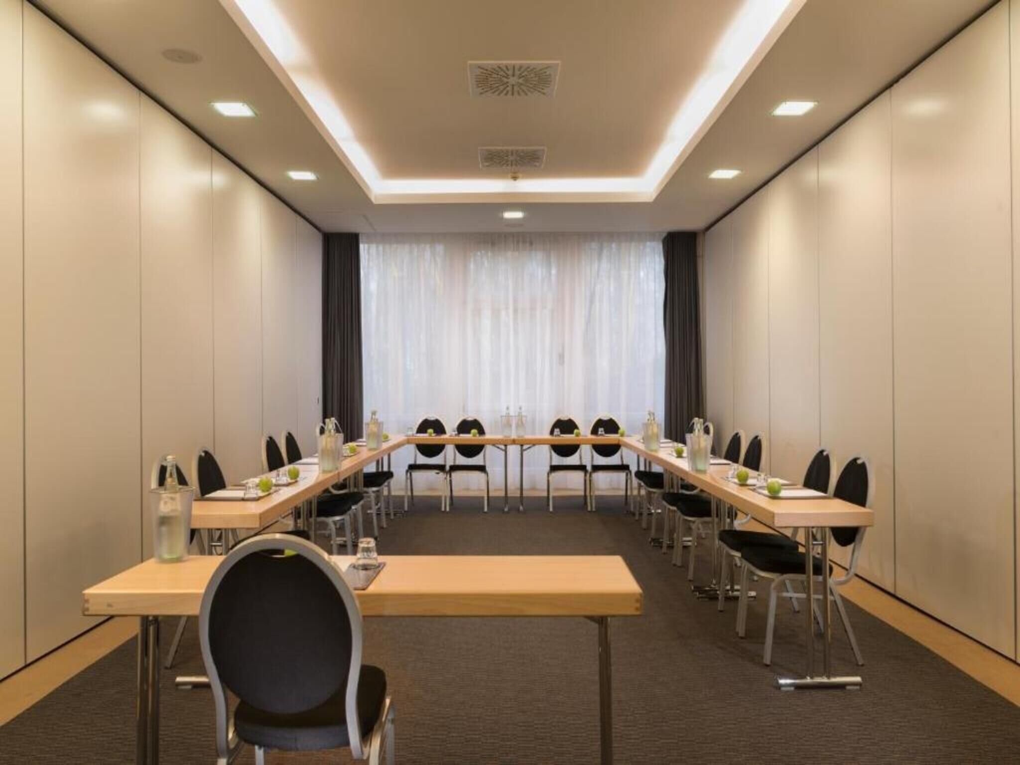 A conference room with a long table, chairs, and a view of a building through large windows.