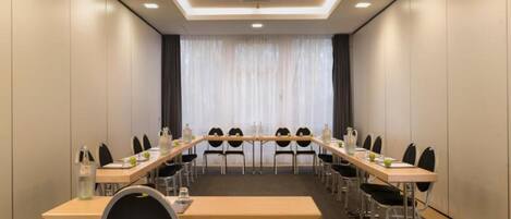 A conference room with a long table, chairs, and a view of a building through large windows.