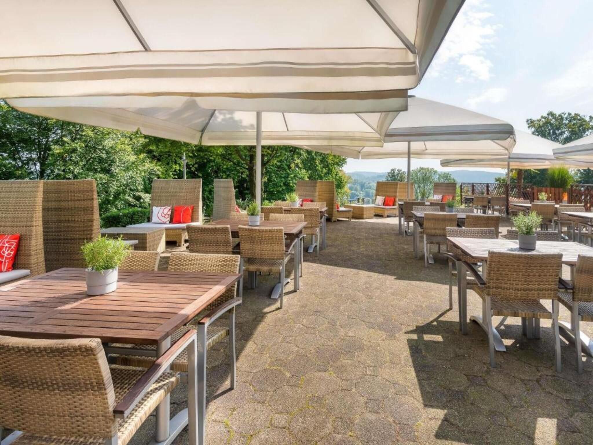 Eine Terrasse im Freien mit Korbmöbeln, Sonnenschirmen und Topfpflanzen.