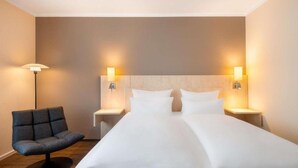 Una habitación de hotel con una cama grande, dos mesitas de noche, una silla y lámparas fijadas a la pared.