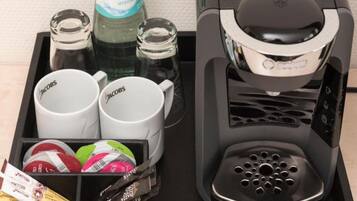 A coffee machine, two coffee mugs, two glass bottles, and a tray with coffee pods and a packet of sugar.