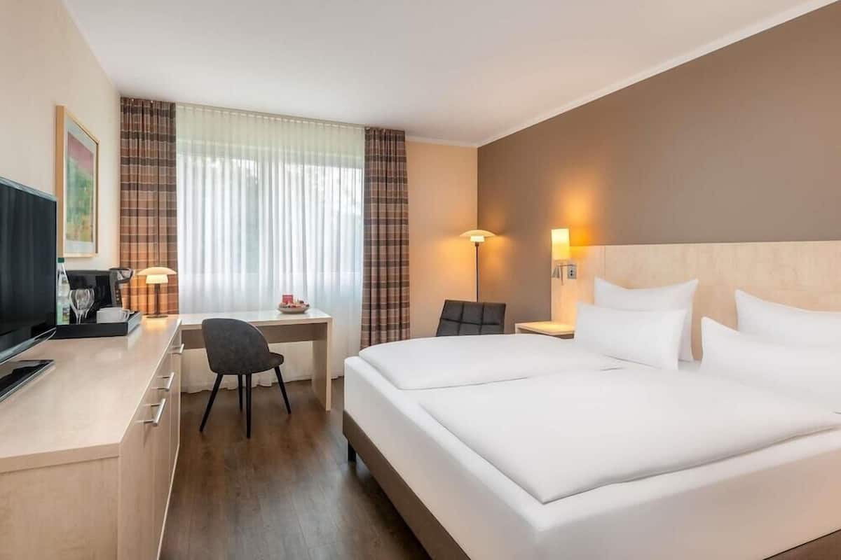 Una habitación de hotel con cama, escritorio, silla, televisor y lámparas.