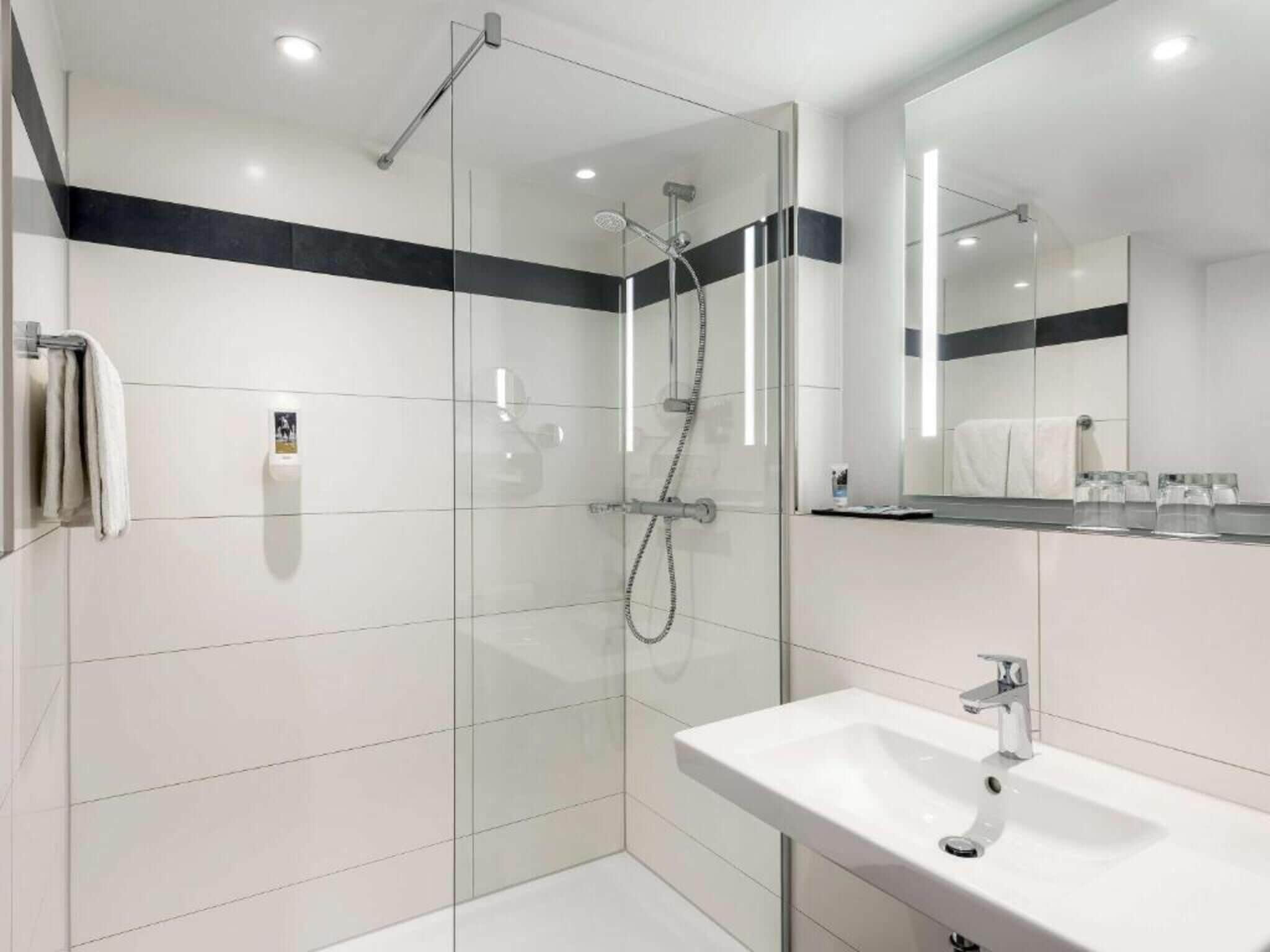 A modern bathroom with a glass-enclosed shower, a white sink, and a large mirror.