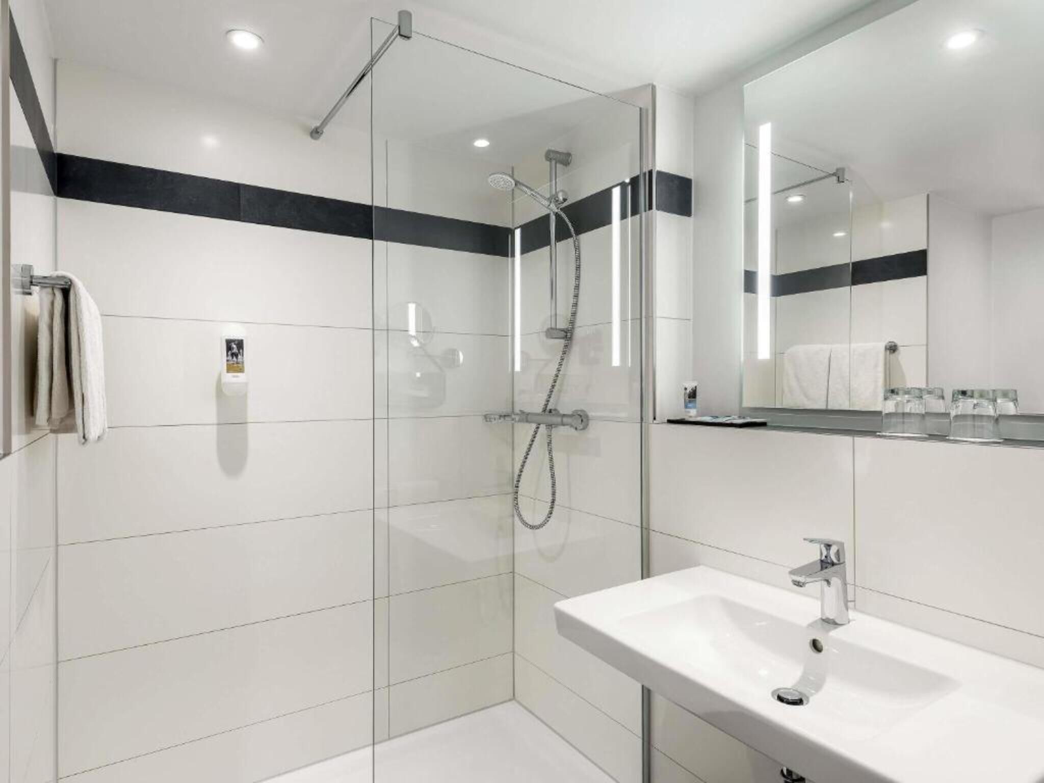 A modern bathroom with a glass-enclosed shower, a white sink, and a large mirror.