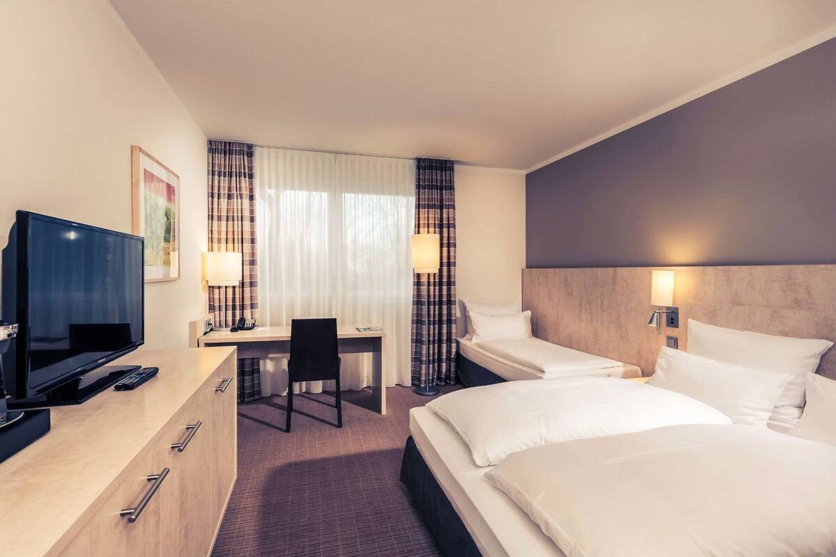 Habitación de hotel con televisión, escritorio, dos camas y cabecero con luz.