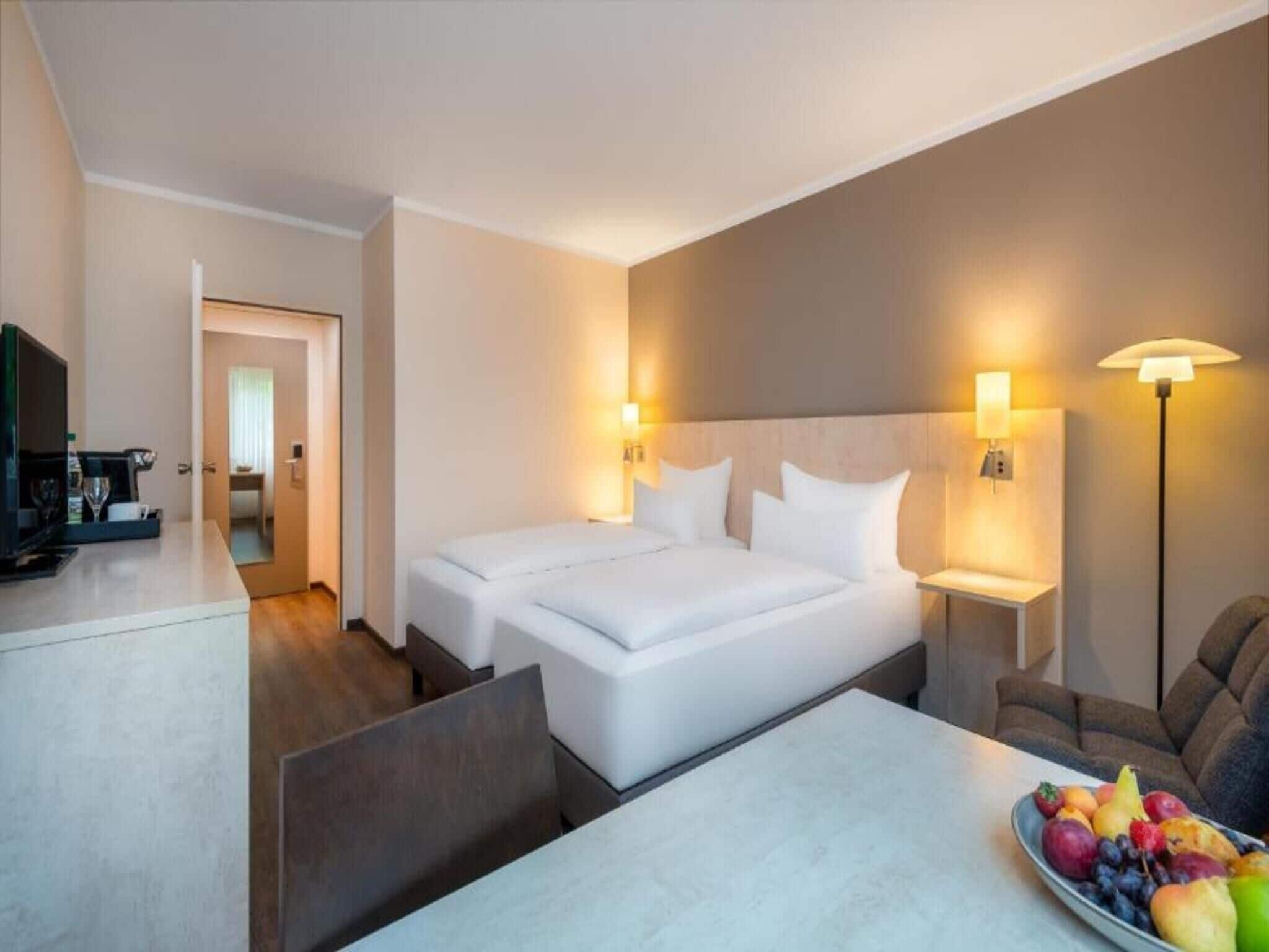 A hotel room with a bed, bedside lamps, a table with fruit, and a TV.