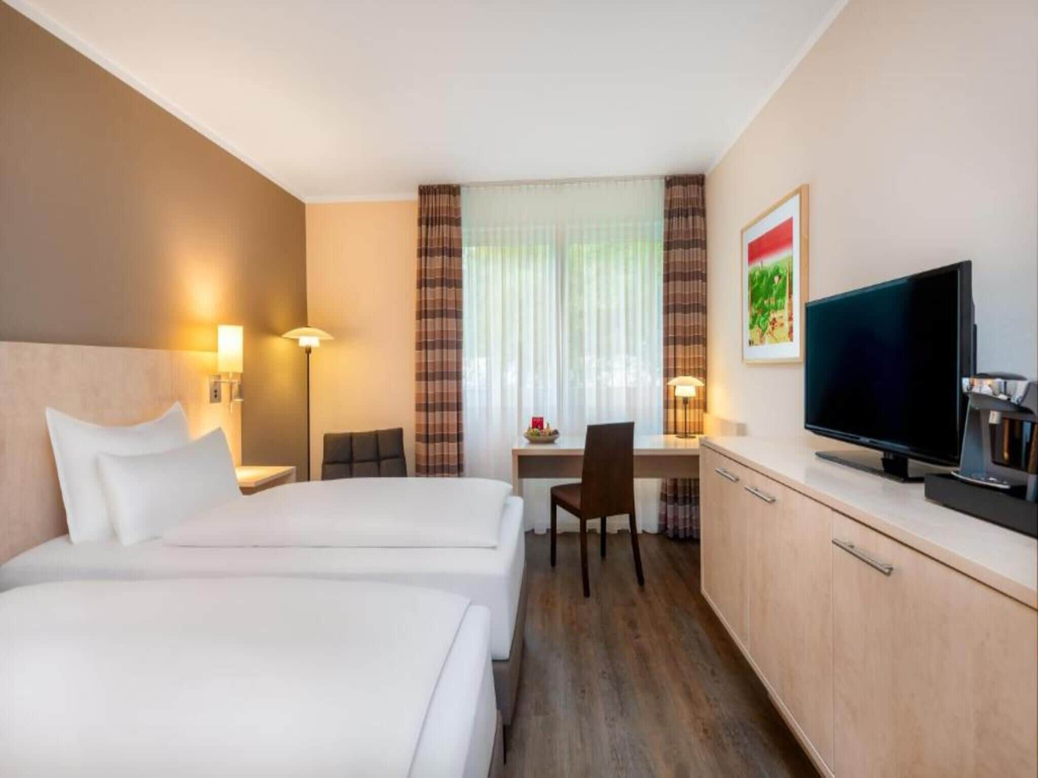 Une chambre d’hôtel avec deux lits, un bureau, une chaise, une télévision et un placard.