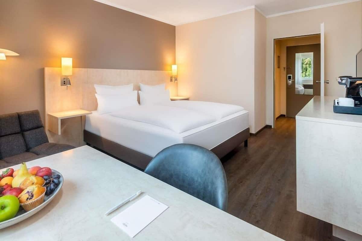 Una habitación de hotel con una cama, mesitas de noche, un escritorio con una silla, un frutero y una cafetera.