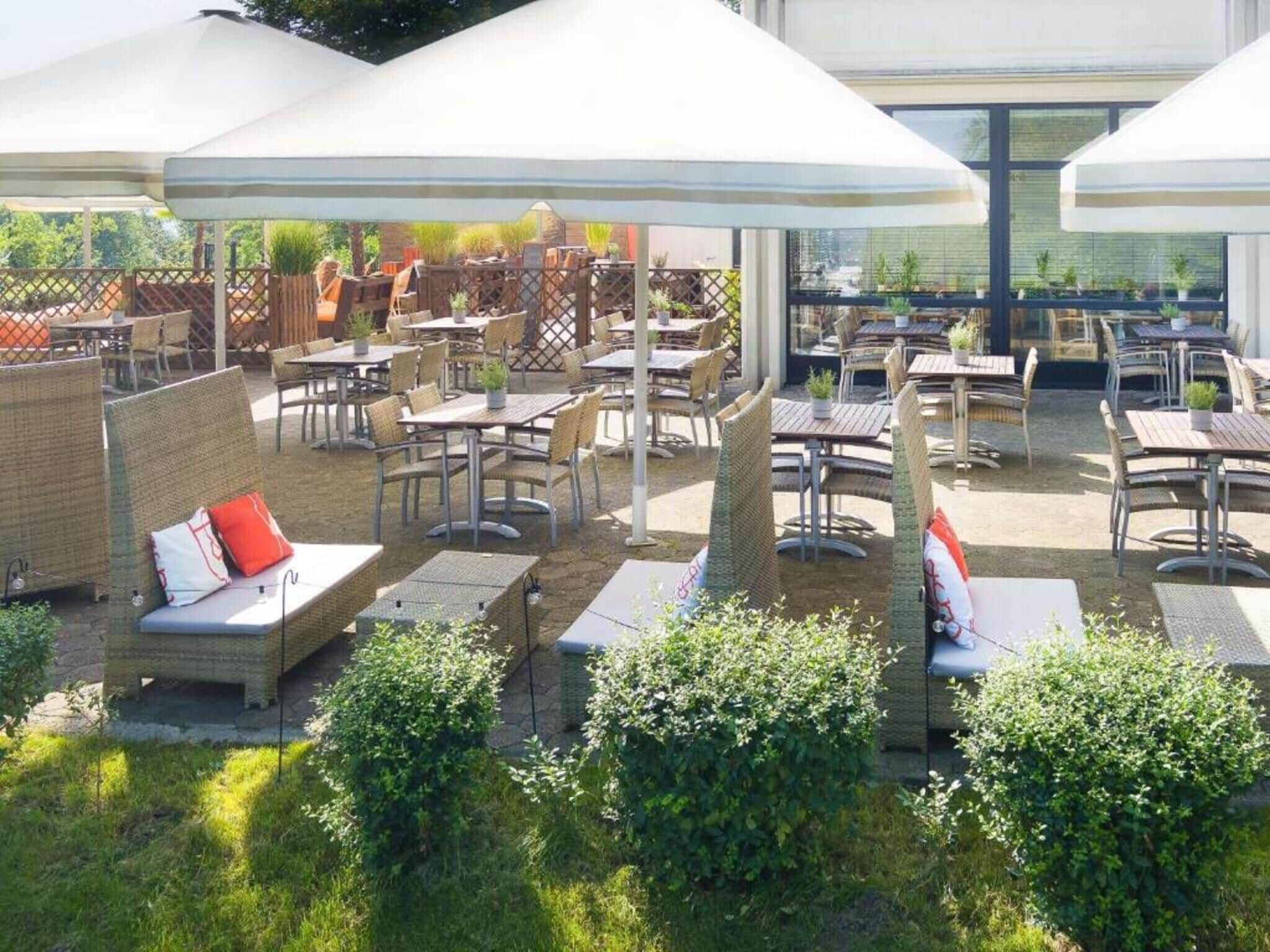 Un patio al aire libre con mesas, sillas, sombrillas y plantas en macetas.