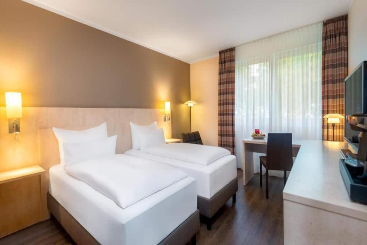 Habitación de hotel con dos camas, un escritorio, una silla y un televisor.