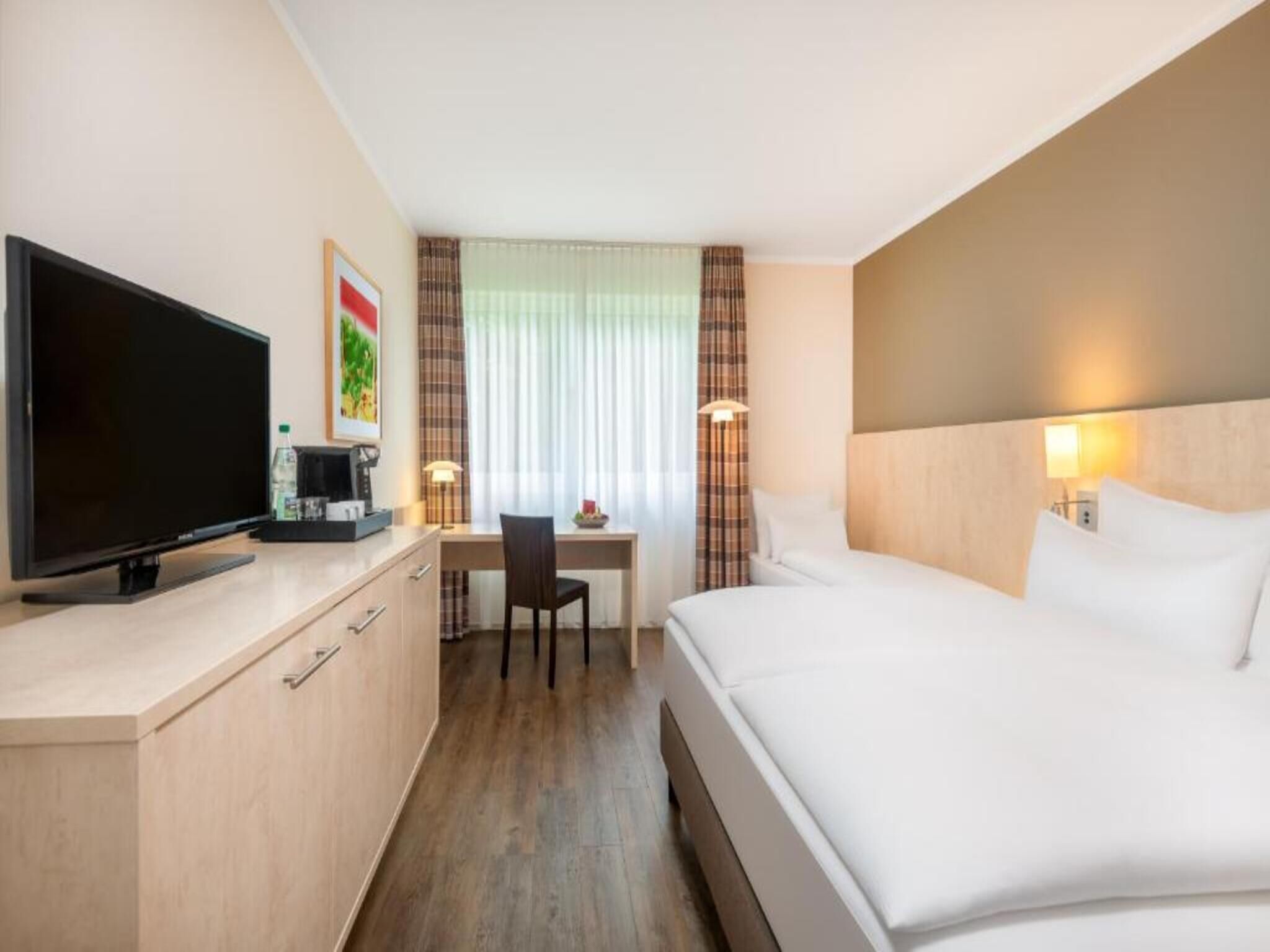 Ein Hotelzimmer mit einem Bett, einem Schreibtisch mit Stuhl, einem Fernseher und einer Kaffeemaschine.