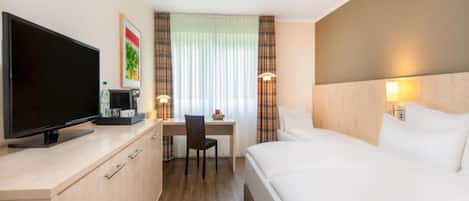 Quarto de hotel com cama, escrivaninha, cadeira, televisão e máquina de café.