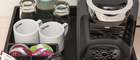 Una cafetera, dos tazas de café, una botella de agua y una bandeja con cápsulas de café.
